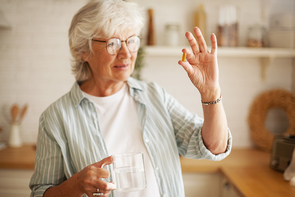 Woman with rheumatoid arthritis looks at vitamin D dietary supplement in her hand.